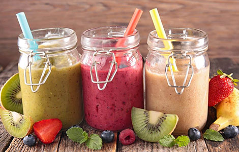 Colorful fruit smoothies in glass jars with fresh kiwi, berries, and 
strawberries on a rustic wooden table at Cream Curls Dunfermline